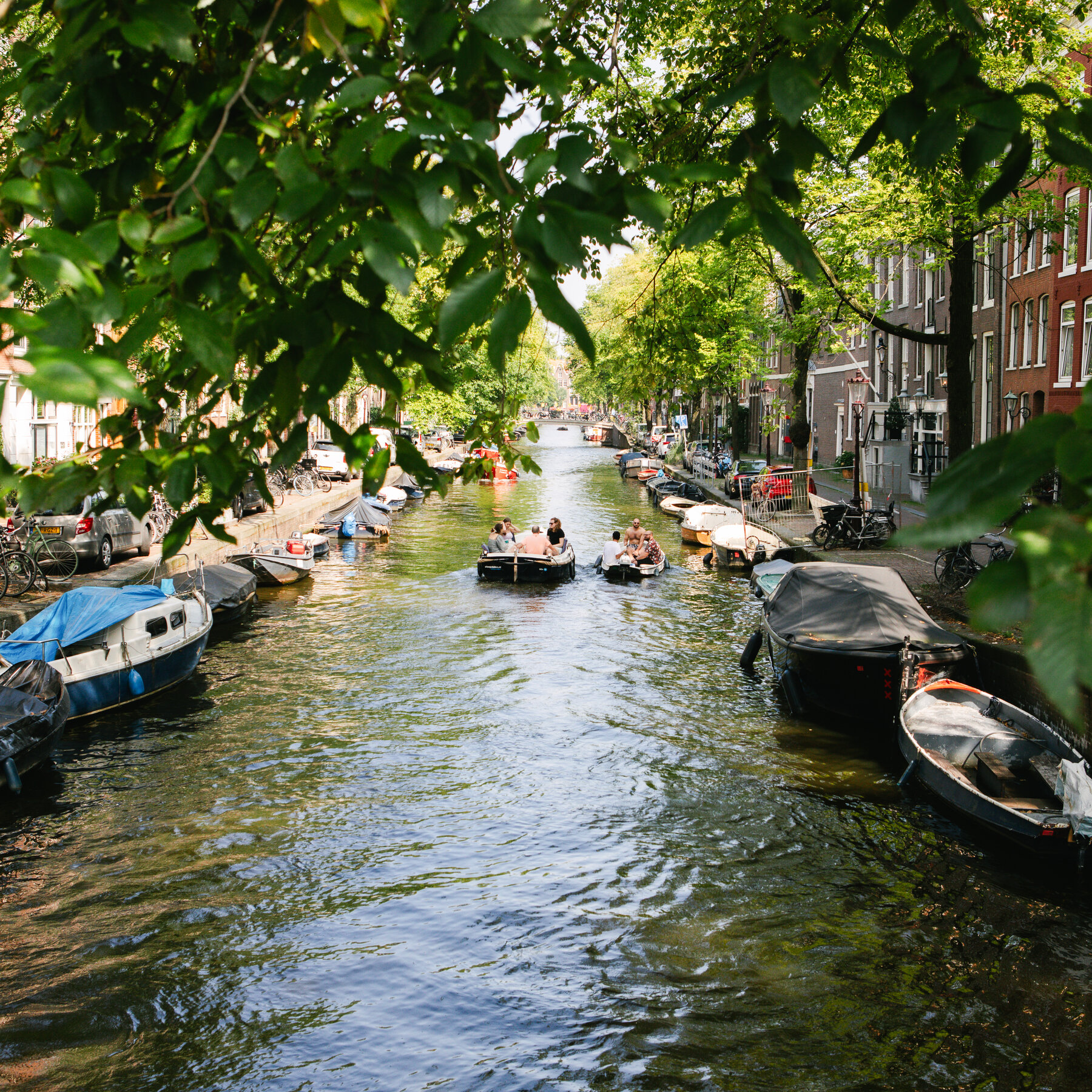 O vedere a unui canal ingust al orasului, cu apa calma, verzuie in timpul zilei.  Oamenii stau in barci in mijlocul apei, iar barci mici sunt ancorate pe maluri.