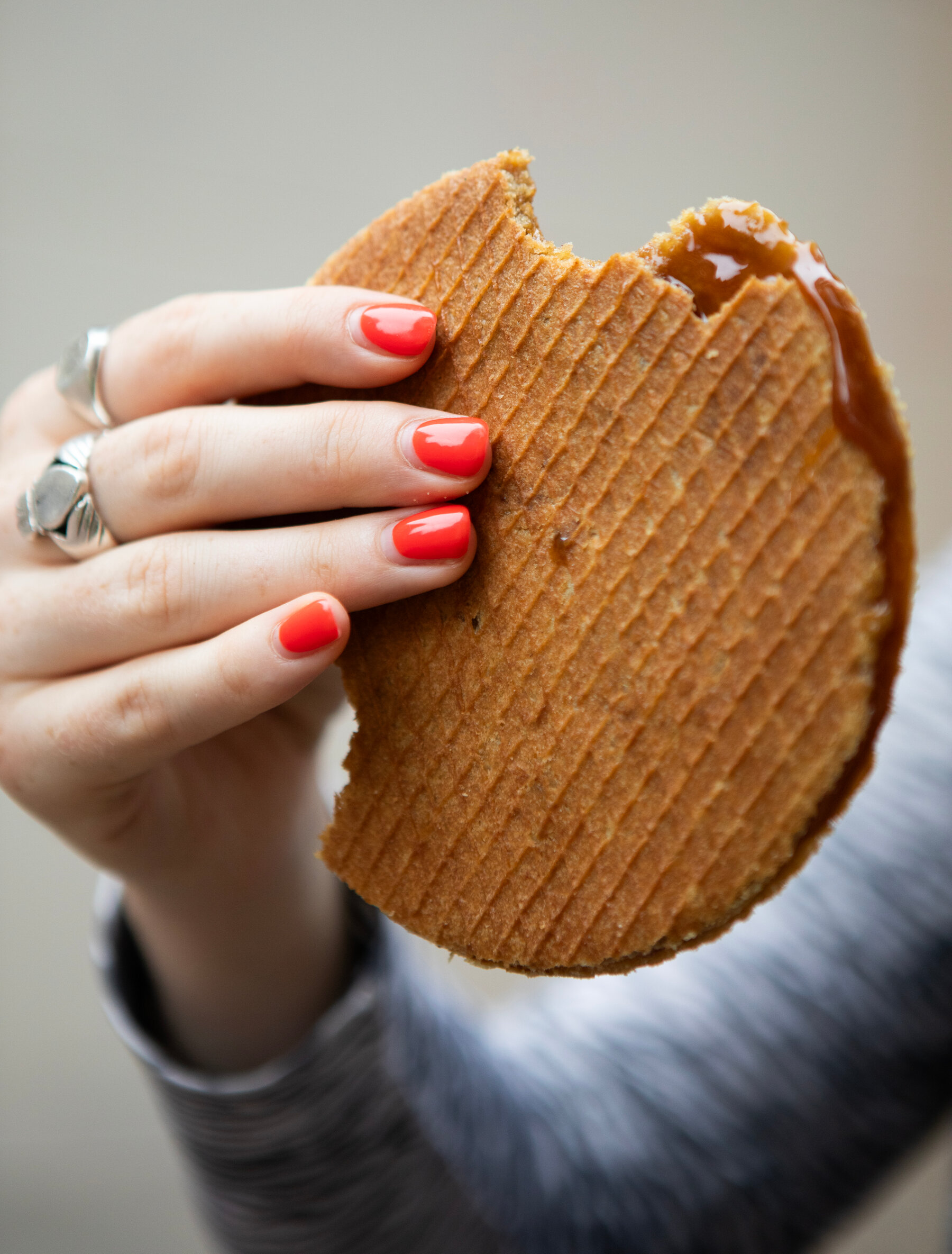O mana cu oja rosie si inele de argint tine un stroopwafel, doua napolitane subtiri cu sirop in mijloc.