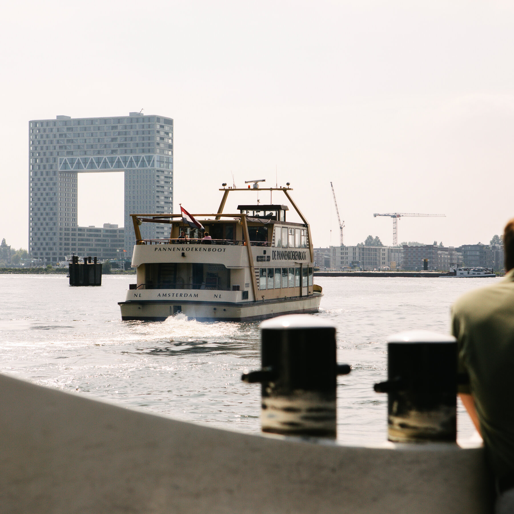 O vedere a unui port in timpul zilei.  Un feribot isi croieste drum peste apa.  O cladire moderna, blocata, care pare sa aiba un patrat taiat prin centru este vizibila in fundal.
